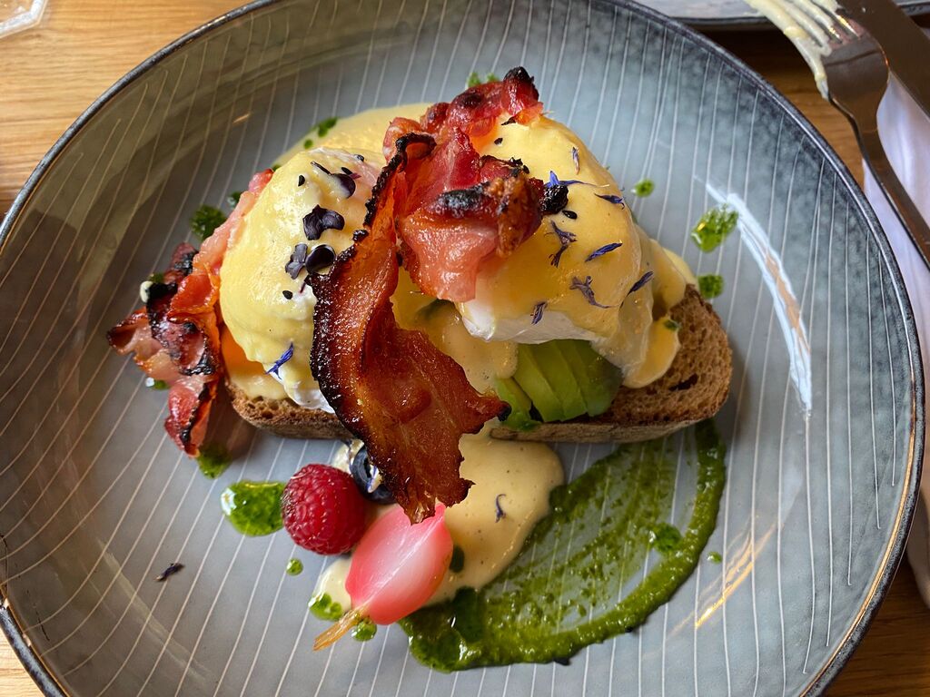Ein kunstvoll angerichtetes Frühstück mit Speck, pochiertem Ei und Avocado auf Brot