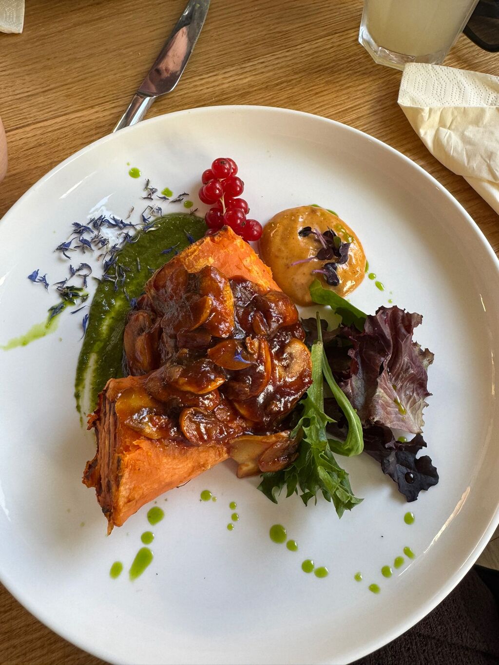 Ein Stück Lasagne mit Pilzsoße, Salat, roten Beeren und cremigem Dip auf weißem Teller