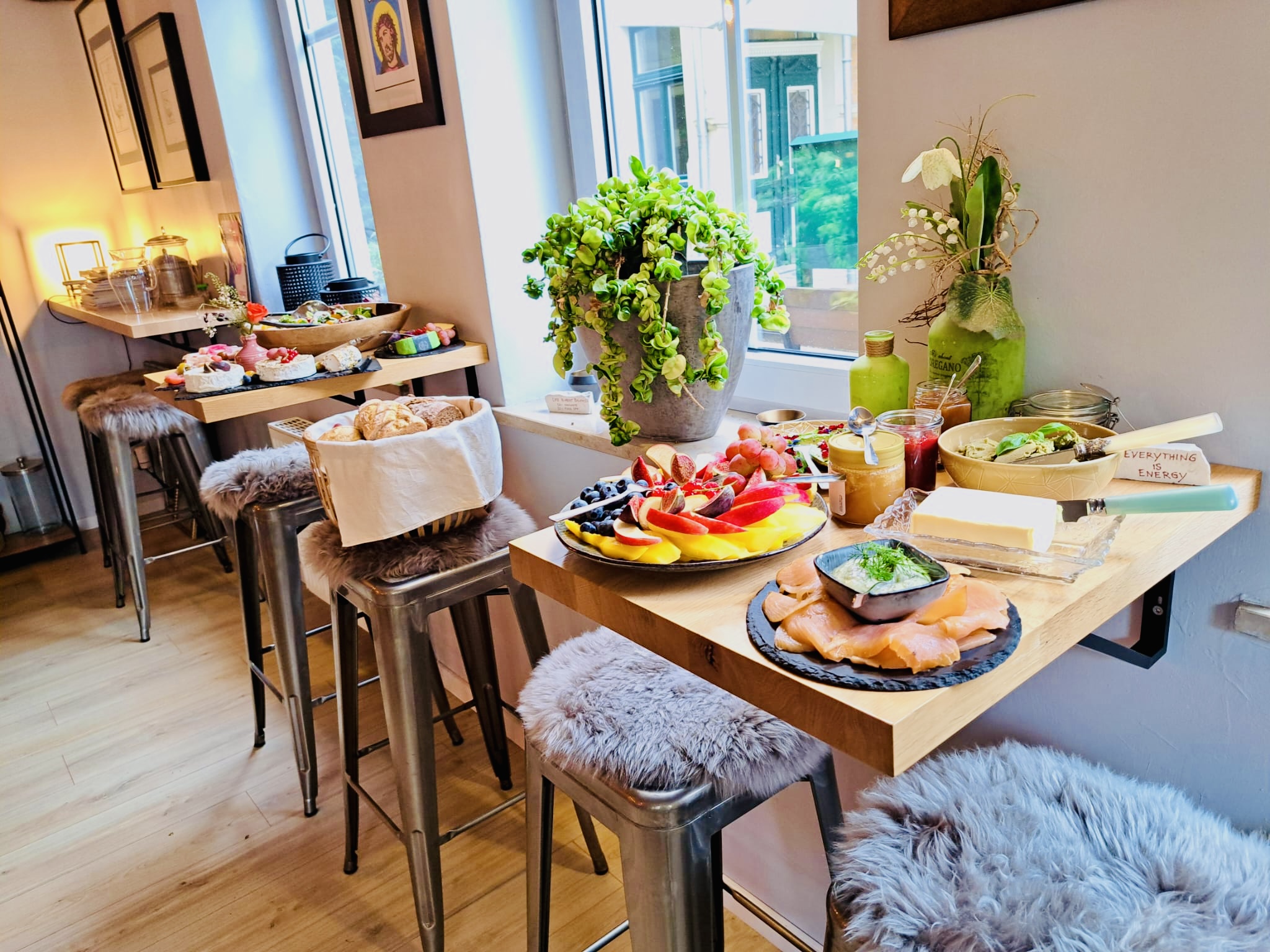 Ein liebevoll gedeckter Frühstückstisch mit buntem Obst und frischem Gebäck steht am Fenster